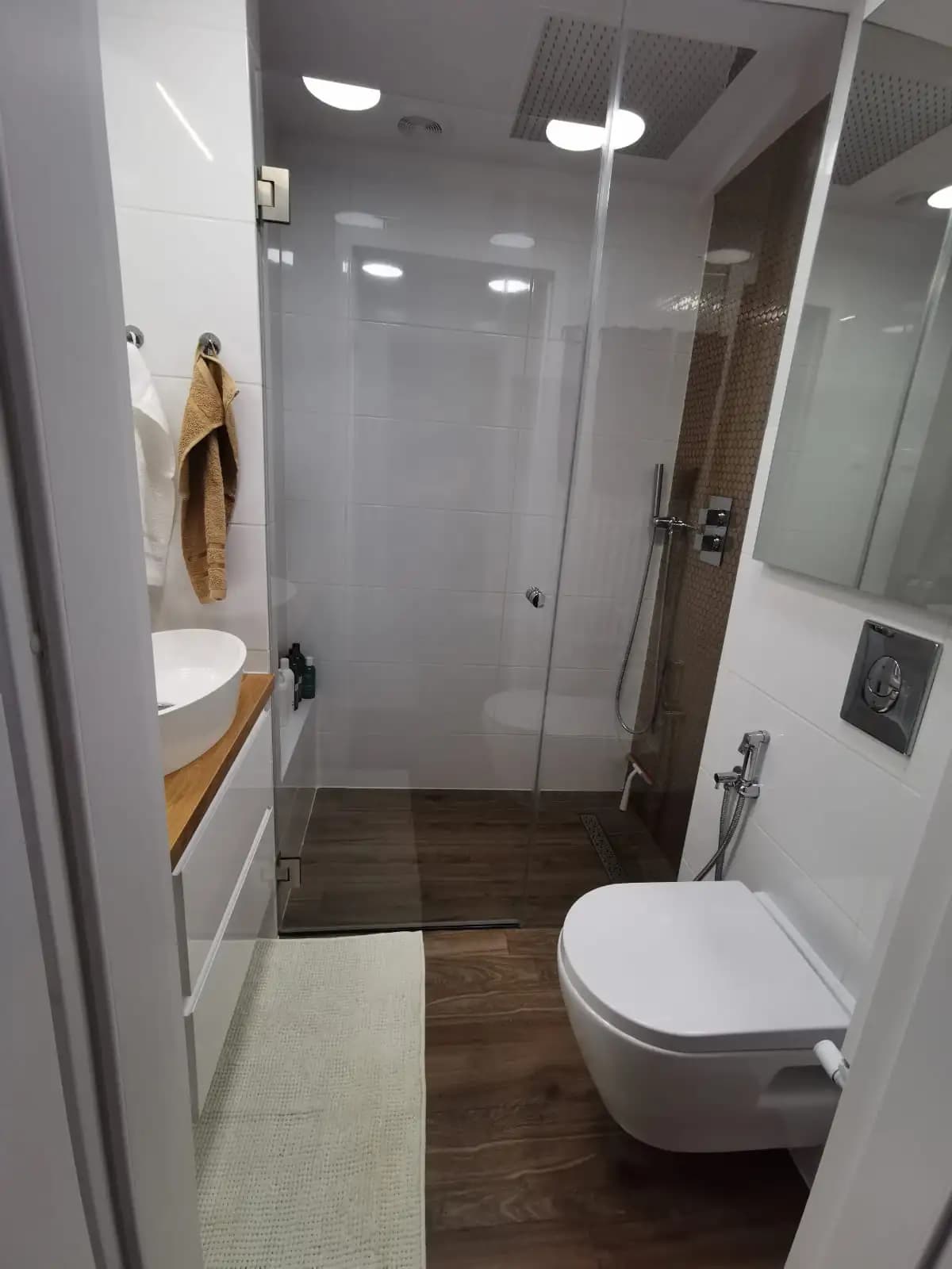 The image shows a bathroom with a toilet on the right and a sink on the left. There's a shower stall in the middle...