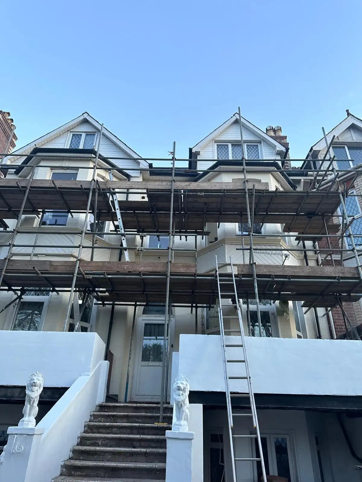 A two-story residential building with a large construction scaffold surrounding it, indicating ongoing renovation...