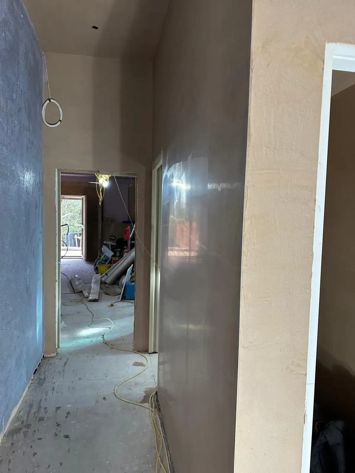 Hallway in a building with plastered walls, a light fixture hanging from ceiling, and doorways on either side.