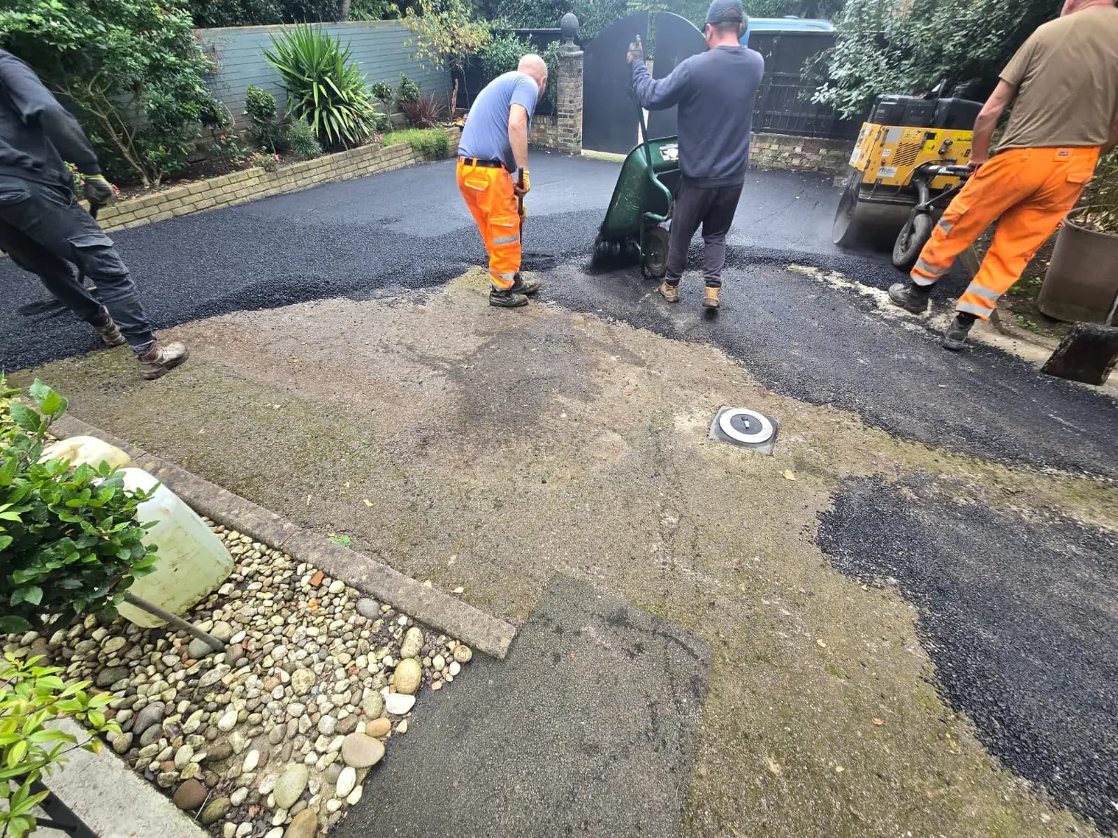 An image of a man in an orange vest inspecting a driveway under construction, with tar applied, in preparation for...