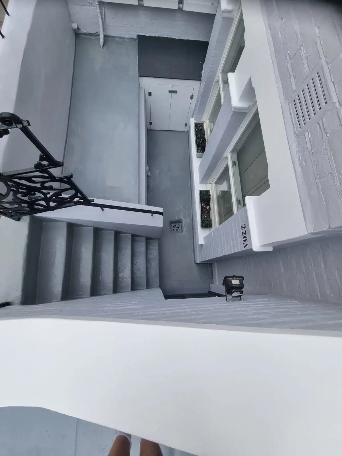 The image shows a multi-story stairwell with light grey walls and white steps. There's a black railing on the right...