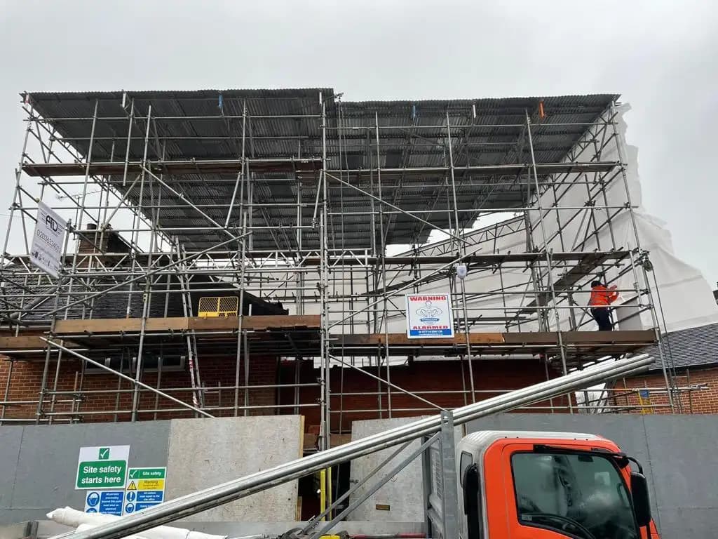 Scaffolding surrounds structure under renovation with tarps on top; construction workers visible amidst materials...