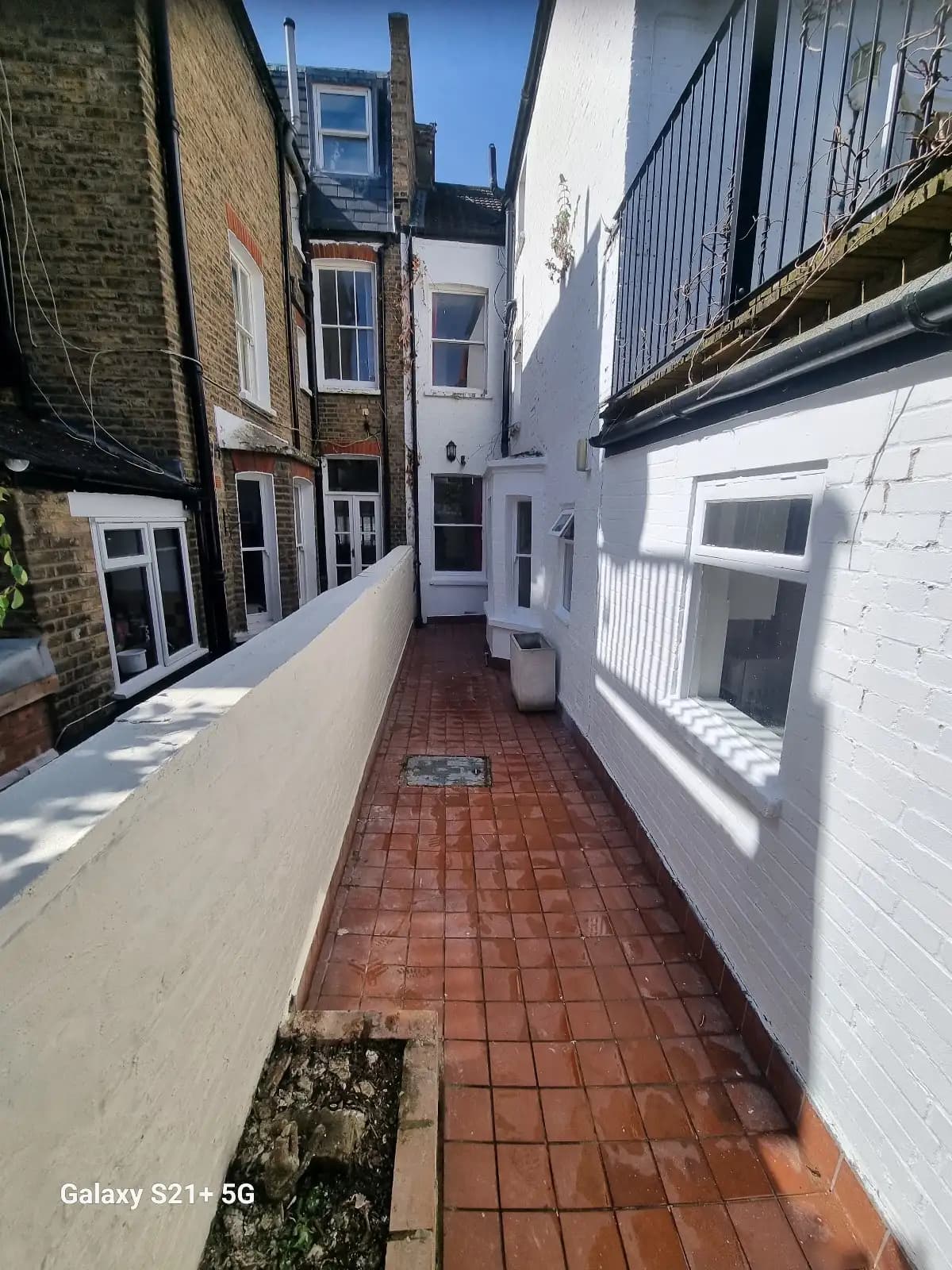 This image shows a narrow street with two-story buildings on either side, featuring white walls and black...